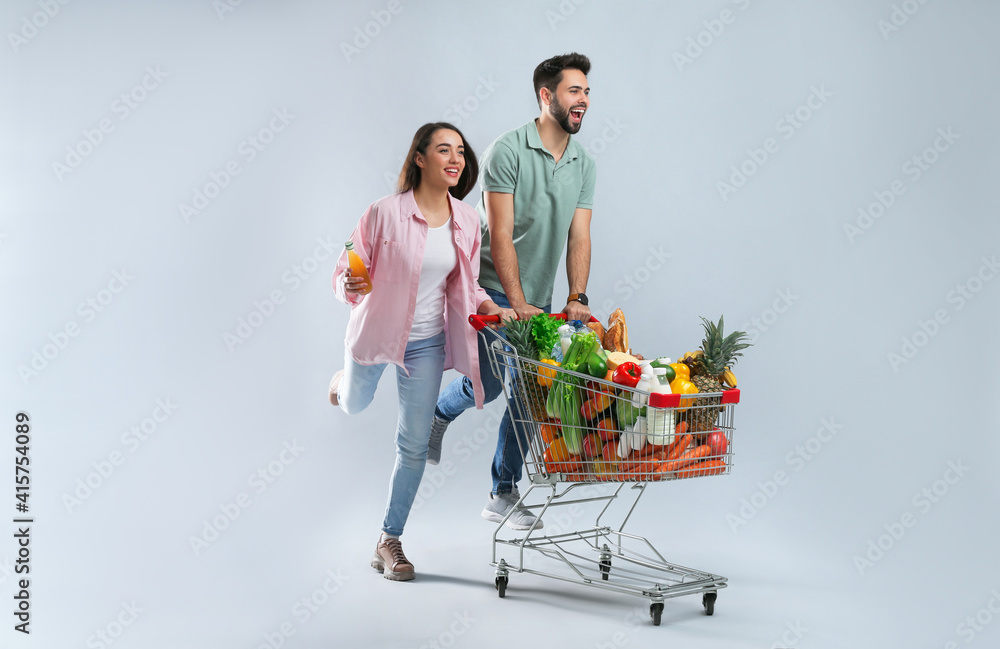 Sticker Young couple with shopping cart full of groceries on grey background