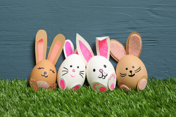 Easter eggs as cute bunnies on green grass against blue wooden background