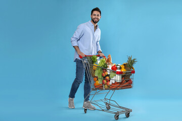 Young man with shopping cart full of groceries on light blue background © New Africa