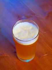 A glass of craft unfiltered light beer on a wooden table, color lighting, top view