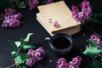 Obraz na płótnie Canvas Spring lilac composition, lilac flowers, blue espresso coffee cup, old books on a black table, romantic greeting card