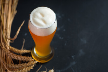 High foamy glass of unfiltered wheat fresh beer on a dark table with a bunch of ears of ripe wheat, copy space