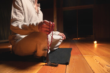 Close up of mens hands with rosary. Young man doing yoga indoors on a black rug. spirituality and practice religion concept