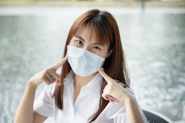 Asian woman pointing and recommending the use of face mask, concept of taking precaution measure, social distancing, new normal lifestyle while waiting for coronavirus cure, COVID-19 vaccine