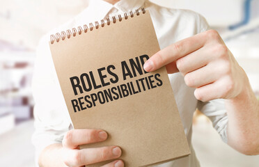 Text roles and responsibilities on brown paper notepad in businessman hands in office. Business...