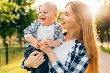 young mom kissing and hugging her baby in the park on a sunny day, Mother's Day,