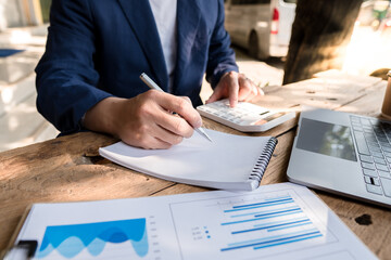 Business accountants are taking notes in notebooks and using a calculator to calculate financial...