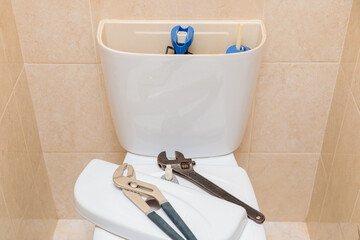 Plumbing tools in the toilet on a white toilet bowl. Drain tank cap removed