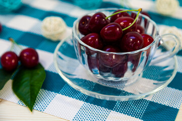 Ripe cherries in a transparent mug on a checkered napkin.