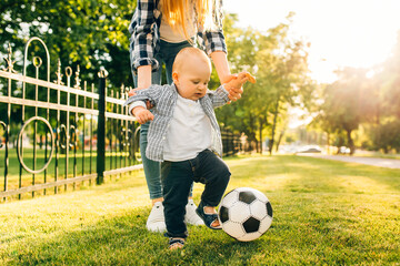 Happy young mom and her little son play soccer together outdoors