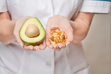 Health care and diet concept - doctor nutritionist or cardiologist holding fish oil in capsules for vitamin D and omega-3 fatty acids and avocado