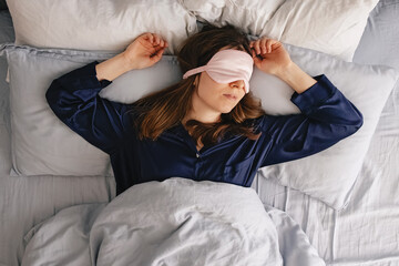 A young woman in a silk sleepwear sleeping in a bed with eyes covered with mask.