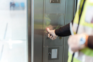 Security man hand in protective glove against coronavirus presses lift buttton.