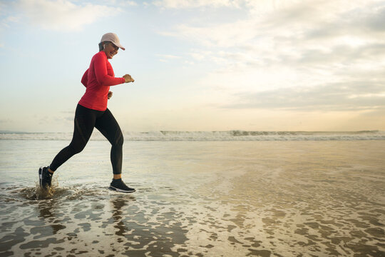 fit and attractive mature woman with grey hair doing beach workout on her 50s running on the beach happy and free in senior fitness selfcare and wellness concept