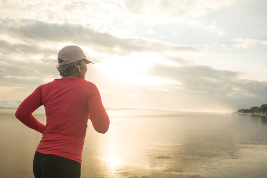 Fit And Attractive Mature Woman With Grey Hair Doing Beach Workout On Her 50s Running On The Beach Happy And Free In Senior Fitness Selfcare And Wellness Concept