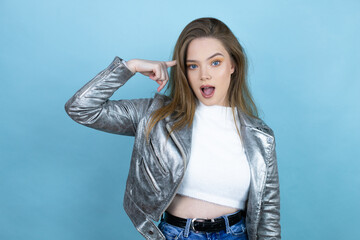 Pretty woman with long hair wearing a casual jacket over blue background surprised and thinking with her finger on her head