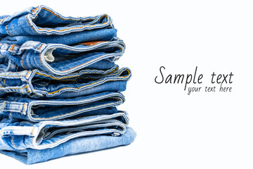 A stack of folded blue jeans close-up with copy space for text on white background, a variety of comfortable casual pants and clothing. Denim cotton fabric with orange thread seams and stitches