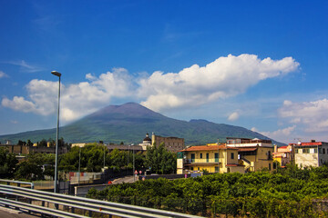 Fototapeta na wymiar Amazing view of Mount Vesuvius on the road from Naples to Pompeii. Campania, southern Italy. The active cone is the high peak on the left side. Soft selective focus, long exposure