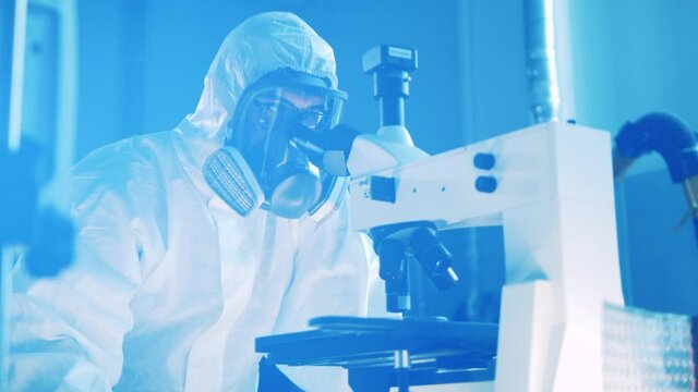 Laboratory specialist in a hazmat suit is operating a microscope. Virus, medicine, science concept.