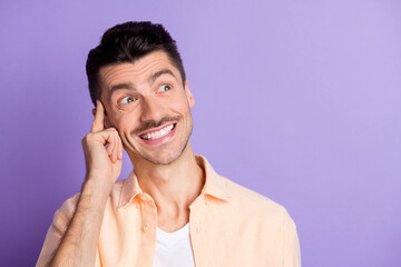 Photo of genius young guy finger temple look up empty space toothy smile wear beige shirt isolated violet color background