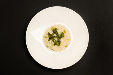 Delicioso risotto con espárragos dentro de un plato blanco redondo sobre un fondo negro. Vista superior. Copy sace