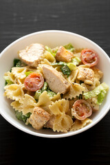 Homemade Chicken Caesar Pasta Salad in a white bowl on a black background, side view. Close-up.