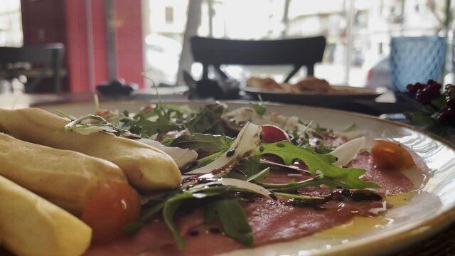 Close-up shot of dining at the restaurant. Having an appetizer with jamon, cheese, rocket salad, dish served together with breadsticks