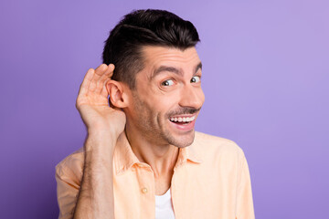 Photo of interested young guy palm ear eavesdropping listen wear beige shirt isolated violet color...