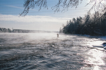 Surfer in a red wetsuit on a board with a paddle floats against the waves. Winter sup surfing on...