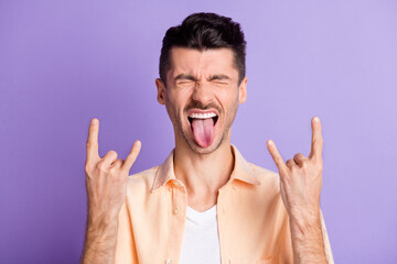 Photo of crazy funky guy eyes closed raise two horn gesture tongue out wear beige shirt isolated violet color background