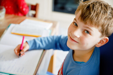 Hard-working happy school kid boy making homework during quarantine time from corona pandemic...