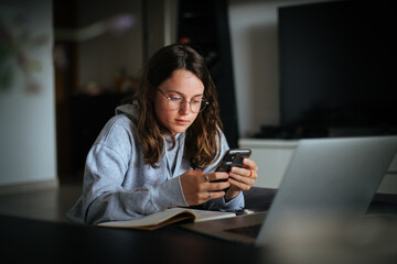Attractive young woman in her 20s look at smartphone in cosy living room. Interaction between generation z and technology natives. Learning app or podcast for youth. Work or study from home