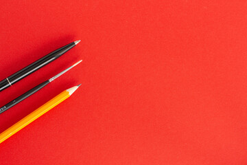 Black pen, pencil and brush on red background