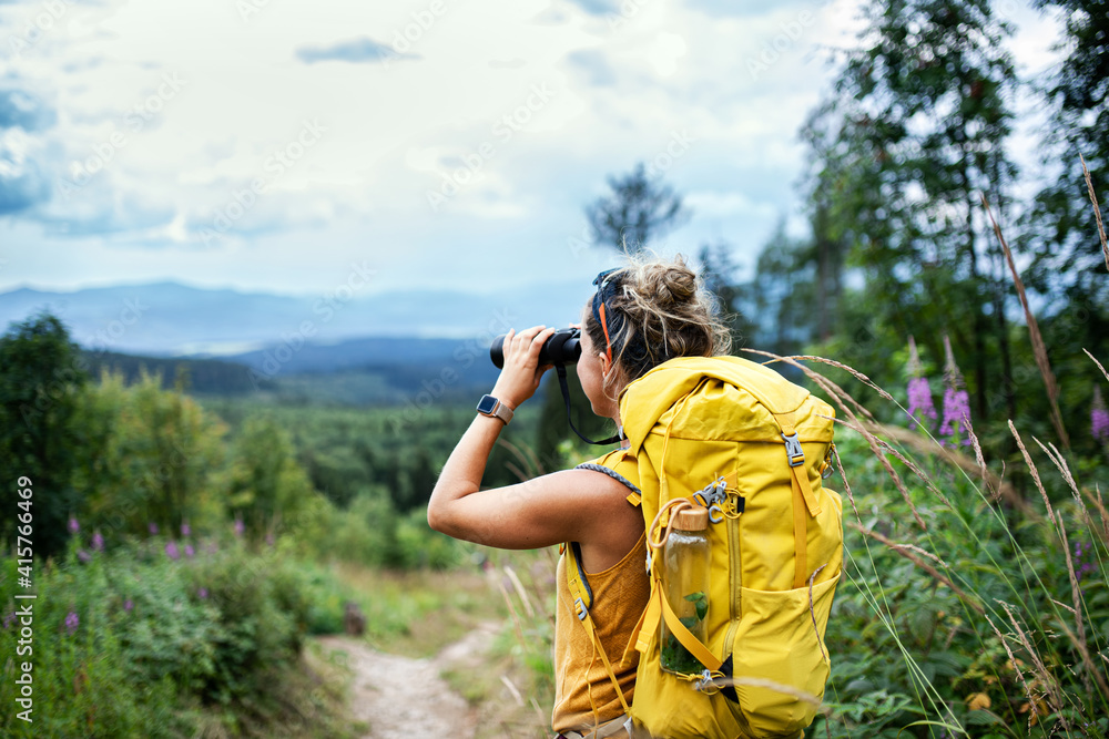 Wall mural rear view of woman hiker with backpack on a hiking trip in nature, using binoculars.