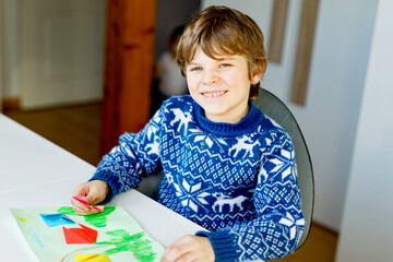 Little kid boy making paper origami tulip flowers for a postcard for mother's day or birthday. Cute child of elementary class school doing handicraft