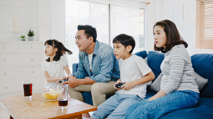 Happy Asia family dad, mom and kids funny playing video game with technology console in living room at house. Self-isolation, stay at home, social distancing, quarantine for coronavirus prevention.