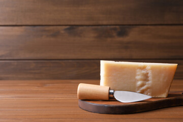 Delicious parmesan cheese with knife on wooden table. Space for text