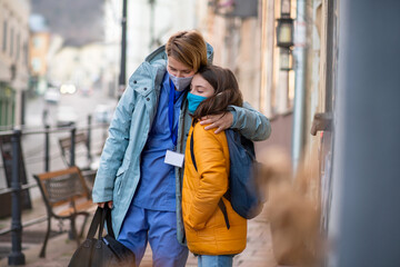 Woman healthcare worker outdoors in town hugging schoolgirl daughter, coronavirus concept.