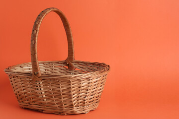 Fototapeta na wymiar Empty wicker basket on coral background, space for text. Easter item
