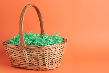 Fototapeta na wymiar Easter basket with green paper filler on coral background, space for text