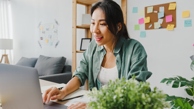 Asia businesswoman using laptop talk to colleagues about plan in video call while smart working from home at living room. Self-isolation, social distancing, quarantine for corona virus prevention.