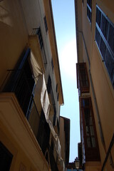 Fototapeta premium Close up outdoor view from above of the top of buildings in a narrow street. Blue sky visible between dark grey walls. Houses facades with windows and shutters.