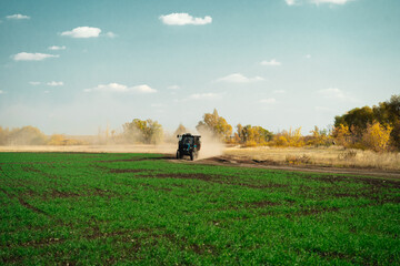 Fototapeta na wymiar A small tractor with a trailer drives through a green overgrown field