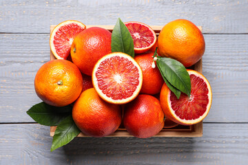 Crate of ripe red oranges and green leaves on grey wooden table, top view