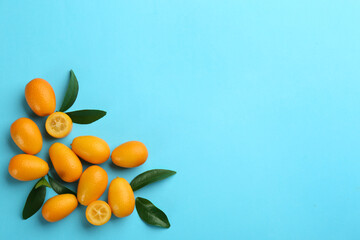 Fresh ripe kumquats with green leaves on light blue background, flat lay. Space for text