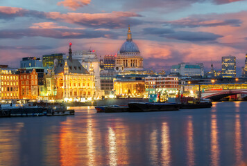 Fototapeta na wymiar Cityscape of London at dusk, view of the famous Saint Pauls Cathedral ans boats on the River Thames illuminated at sunset.