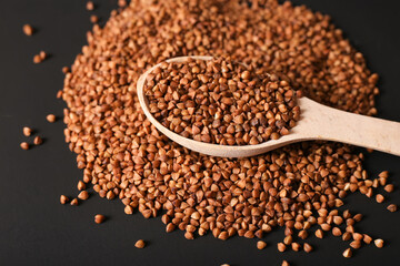 Handful of buckwheat in an iron spoon on a dark background