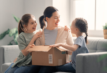 Mother and daughters are unpacking cardboard - obrazy, fototapety, plakaty