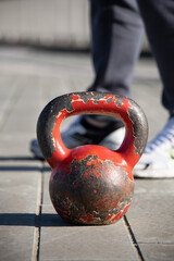 Fototapeta na wymiar Close up shot of an old, very used red gym iron ball on a paved flloor. Outdoor training session due to covid restrictions and gym closures in Italy. Trainer's feet in the background.