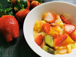 Bowl of fresh fruit salad surrounded by assortments of freshly prepared fruits.